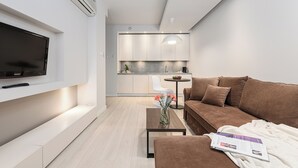 Egy modern nappali, melyben található egy síkképernyős televízió, egy kanapé, egy dohányzóasztal és egy újság.