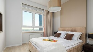 Egy modern hálószoba, melyben egy nagy ágy, függönnyel ellátott ablak, egy éjjeliszemélyzet lámpával és kilátás nyílik a városra.
