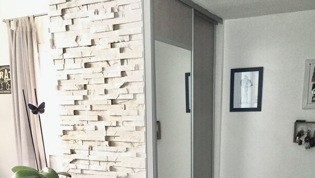 A modern room with a white brick accent wall, a sliding door, a small plant on a white console table, and a framed picture on the wall.