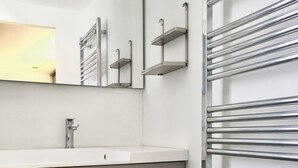 A bathroom with a white sink, wooden cabinet drawers, a mirror, and a metal towel rack.