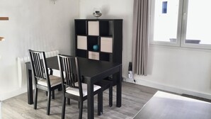 A dining area with a black table and chairs, a black and white bookshelf, and a window with curtains.
