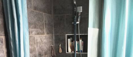 Une salle de bain avec douche, toilettes et une étagère contenant des articles de toilette.