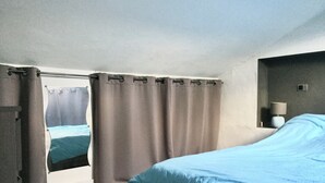 A bedroom with a bed, curtains, a nightstand with a lamp, and a view through the curtains.