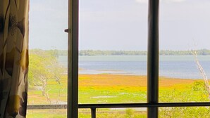 A room with a large window overlooking a lake and a distant shoreline. - Wanamal Lake Front Yala (Tissamaharama)