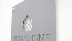 Une plaque métallique portant l’inscription « VICOLOHOME » et le logo stylisé d’une maison, fixée à un mur.