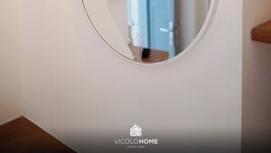 Un miroir rond est fixé sur un mur blanc, et un luminaire en bois est placé au-dessus.