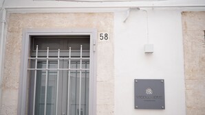 Une façade d’immeuble avec une fenêtre ornée d’une grille métallique, une enseigne portant le numéro « 58 » et une plaque avec les inscriptions « VICOLOHOME » et « VIA NUOVA 56/58 ».