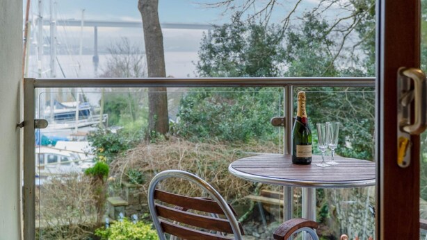 A table with a bottle of Moët & Chandon champagne and two glasses, overlooking a marina with boats and greenery. - Marina House Annex - 1 Bedroom - Neyland (Milford Haven)