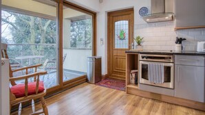 A modern kitchen with a large window, a wooden door with a ship decoration, and a view of trees outside. - Marina House Annex - 1 Bedroom - Neyland (Milford Haven)