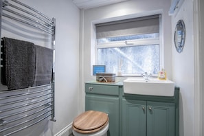 A bathroom with a toilet, a sink, a window, and a towel rack. - Stable Cottage - 1 Bedroom Cottage - Penally (Tenby)