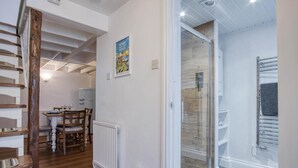 A modern interior with a dining area, a glass shower enclosure, and a staircase. - Stable Cottage - 1 Bedroom Cottage - Penally (Tenby)