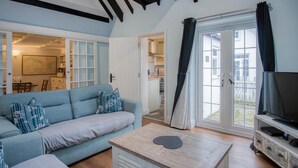 A living room with a light blue sofa, a wooden coffee table, and a television on a wooden stand. - Stable Cottage - 1 Bedroom Cottage - Penally (Tenby)
