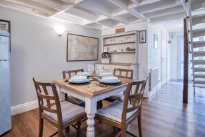 A dining area with a wooden table set for four, surrounded by chairs with striped cushions. A map is displayed on the wall above the table. - Stable Cottage - 1 Bedroom Cottage - Penally (Tenby)