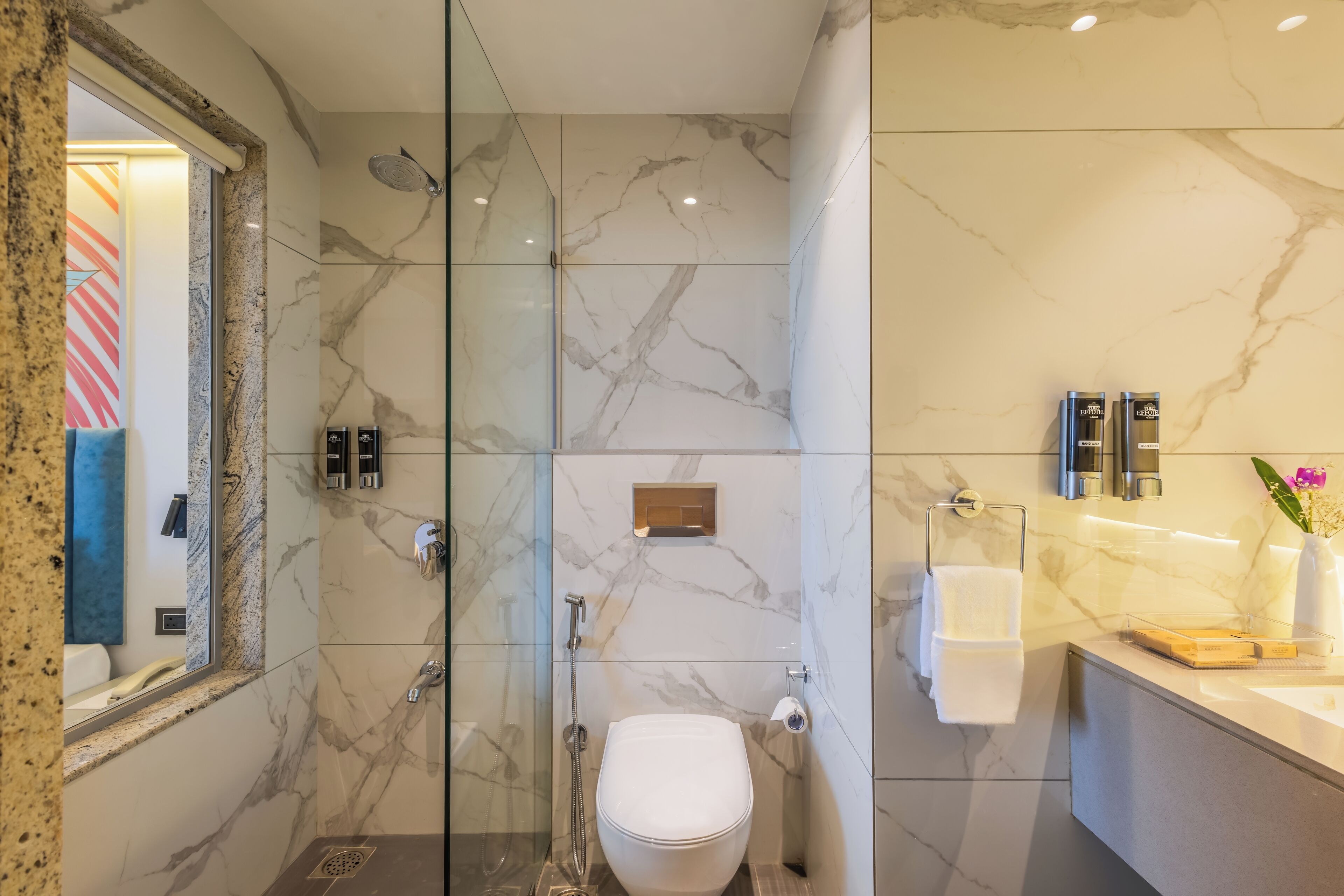 Une salle de bain moderne avec une douche à parois de verre, des toilettes blanches et un mur recouvert de carreaux de marbre.