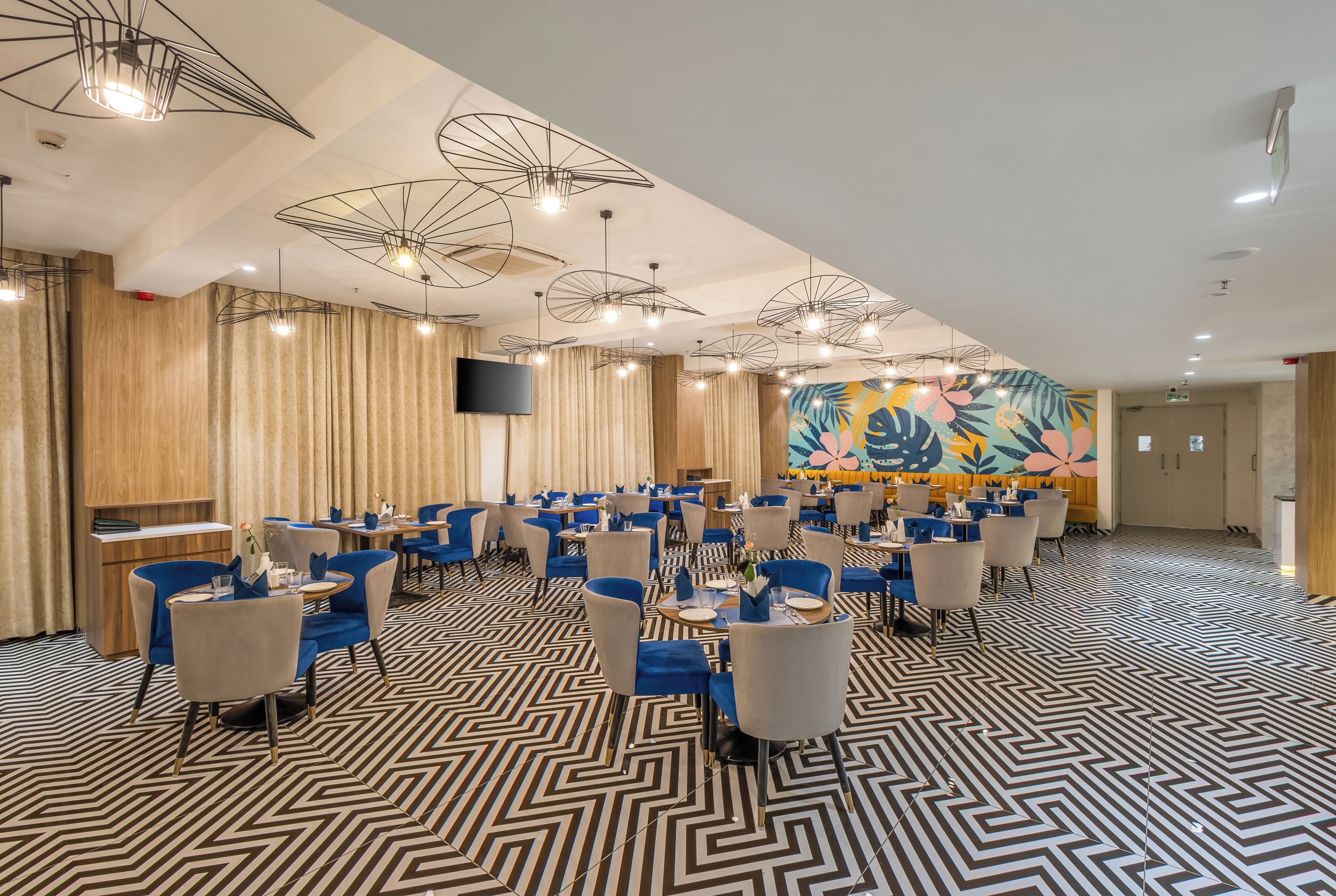 A spacious dining area with modern chairs and tables, a patterned floor, and a large mural on the wall.