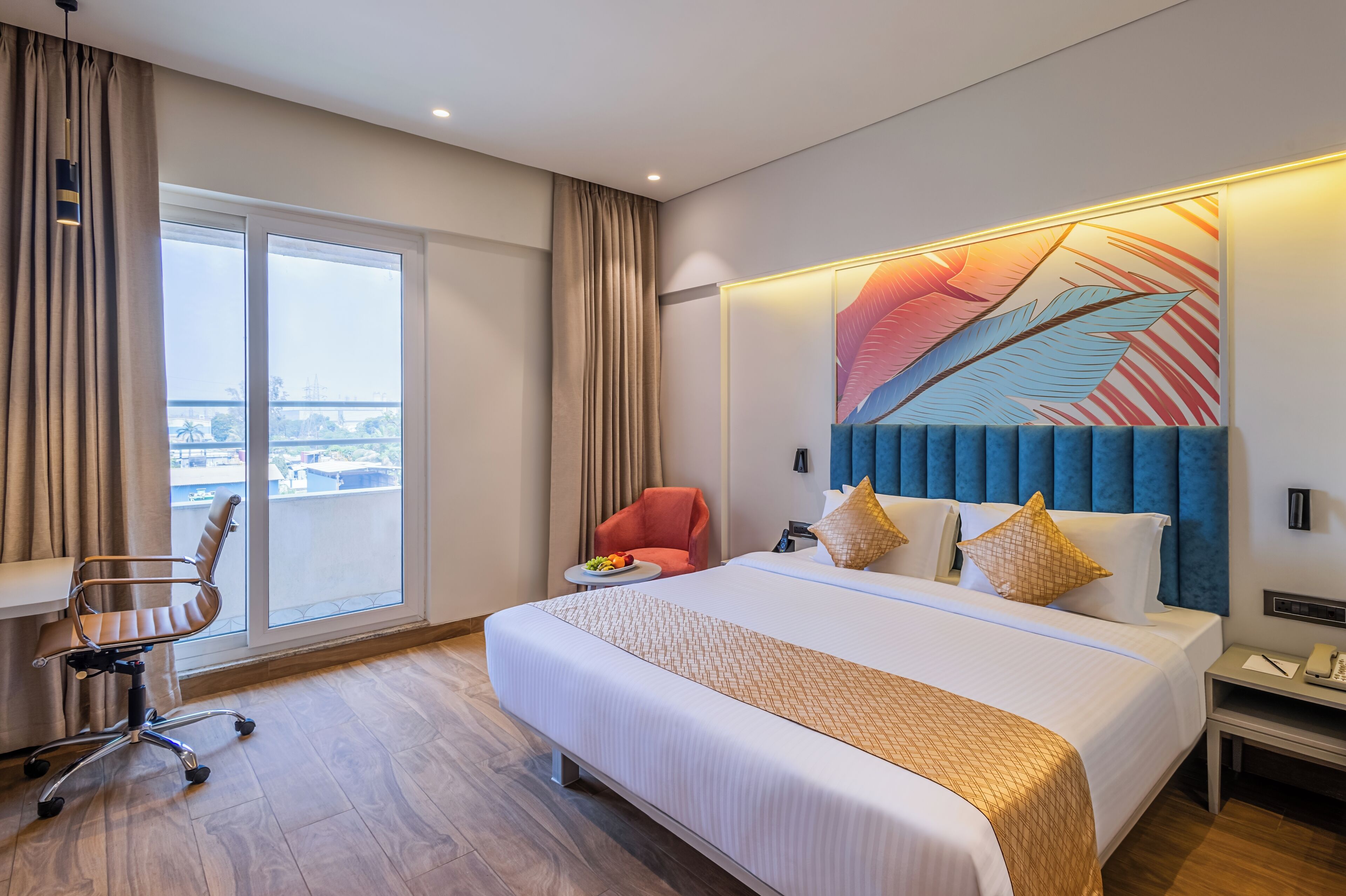 A hotel room with a large bed, a desk, a chair, and a view of the city through a large window.