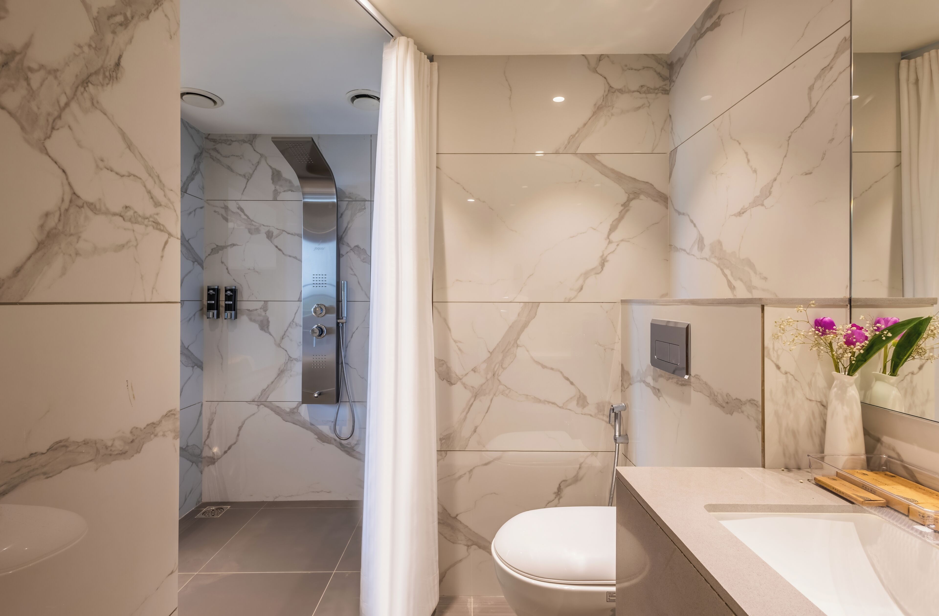 Un baño moderno con paredes de mármol, una ducha, un inodoro y un tocador con espejo y un florero.