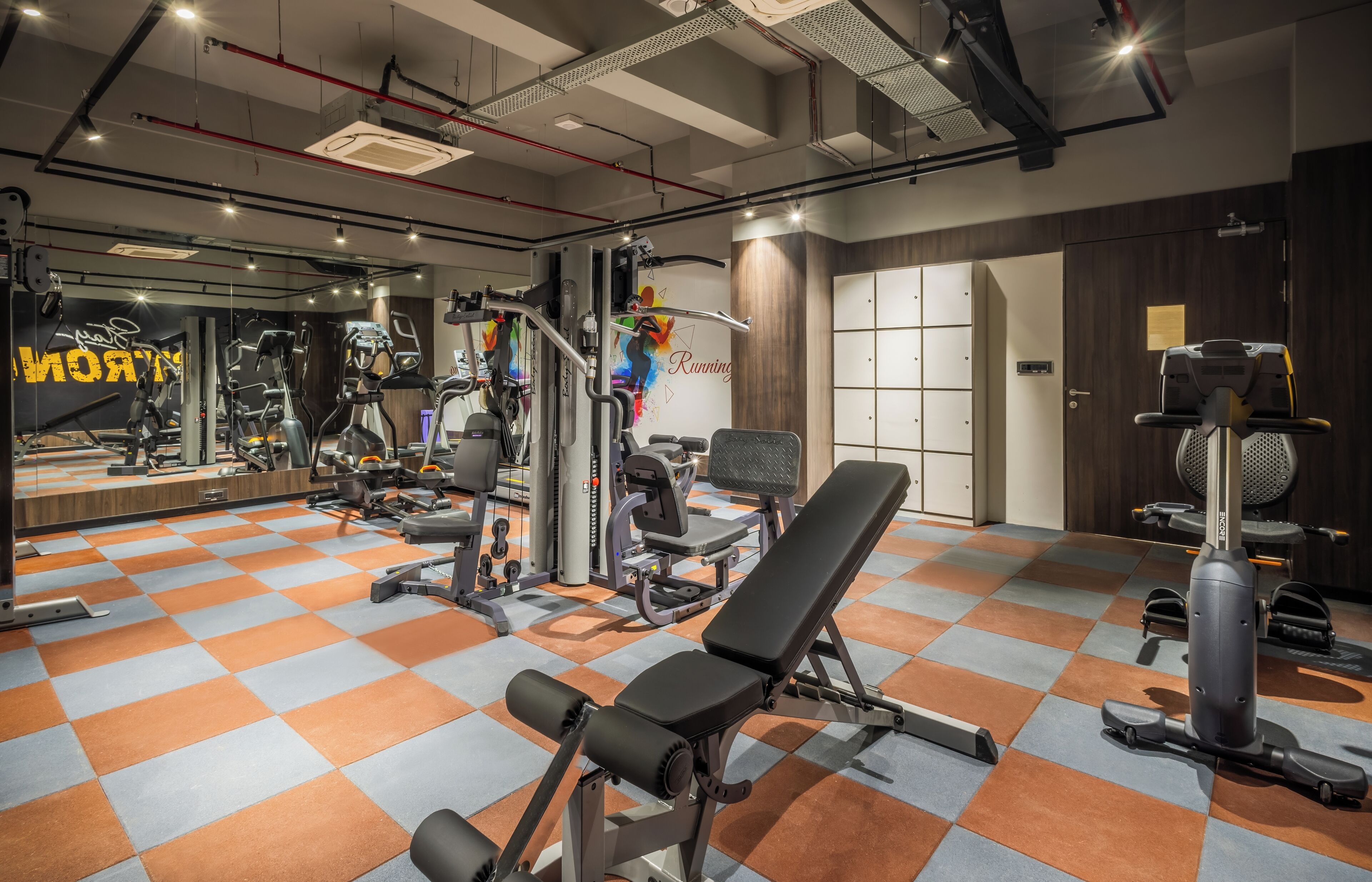 A gym with various exercise equipment, a mirrored wall, and a checkered floor pattern.