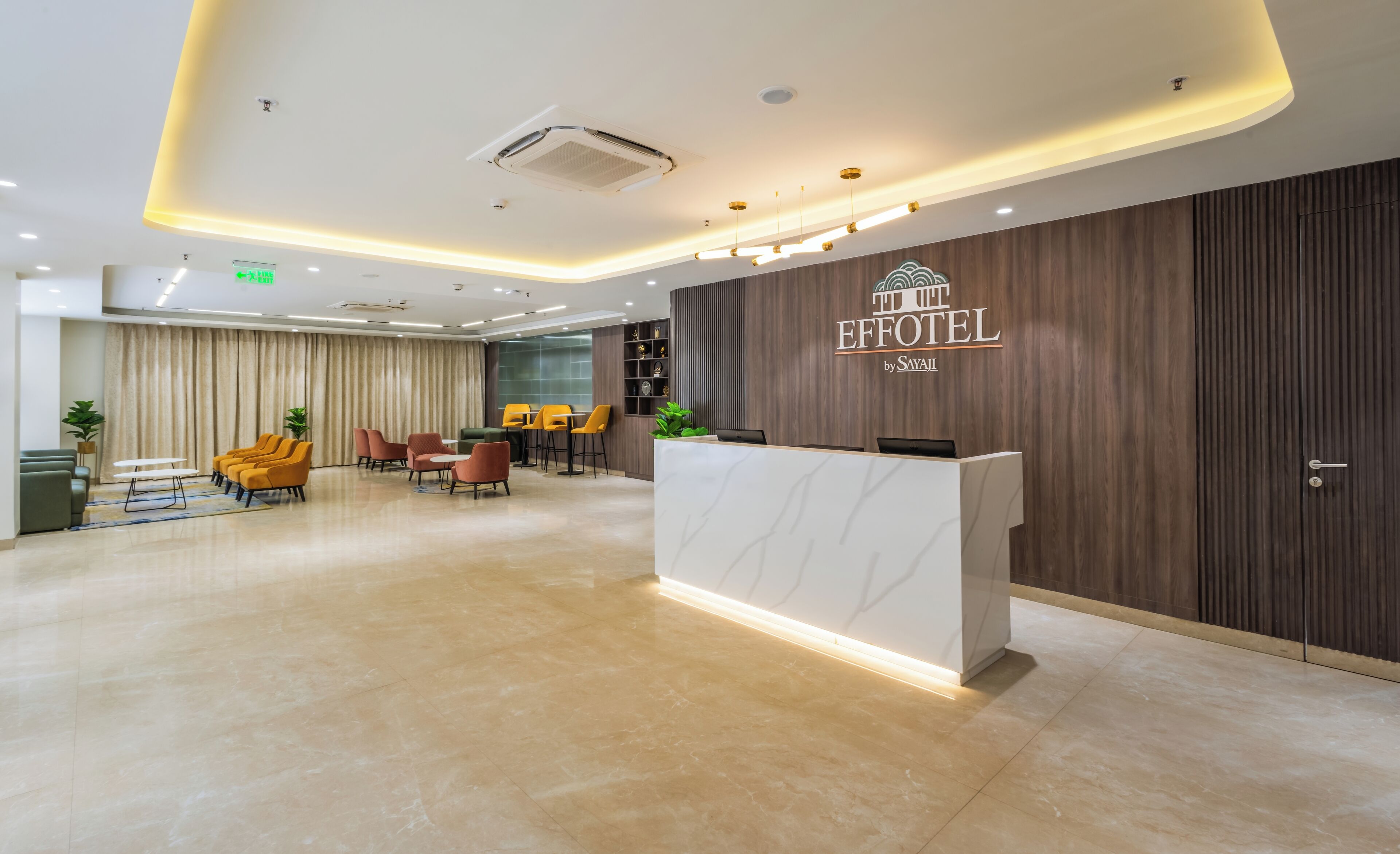 A hotel reception area with a marble reception desk, a seating area with chairs, and a wall with a sign that reads "The Effotel by Savaji".