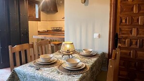 Un coin repas avec une table dressée pour quatre personnes, une porte en bois rustique et une cuisine en arrière-plan.