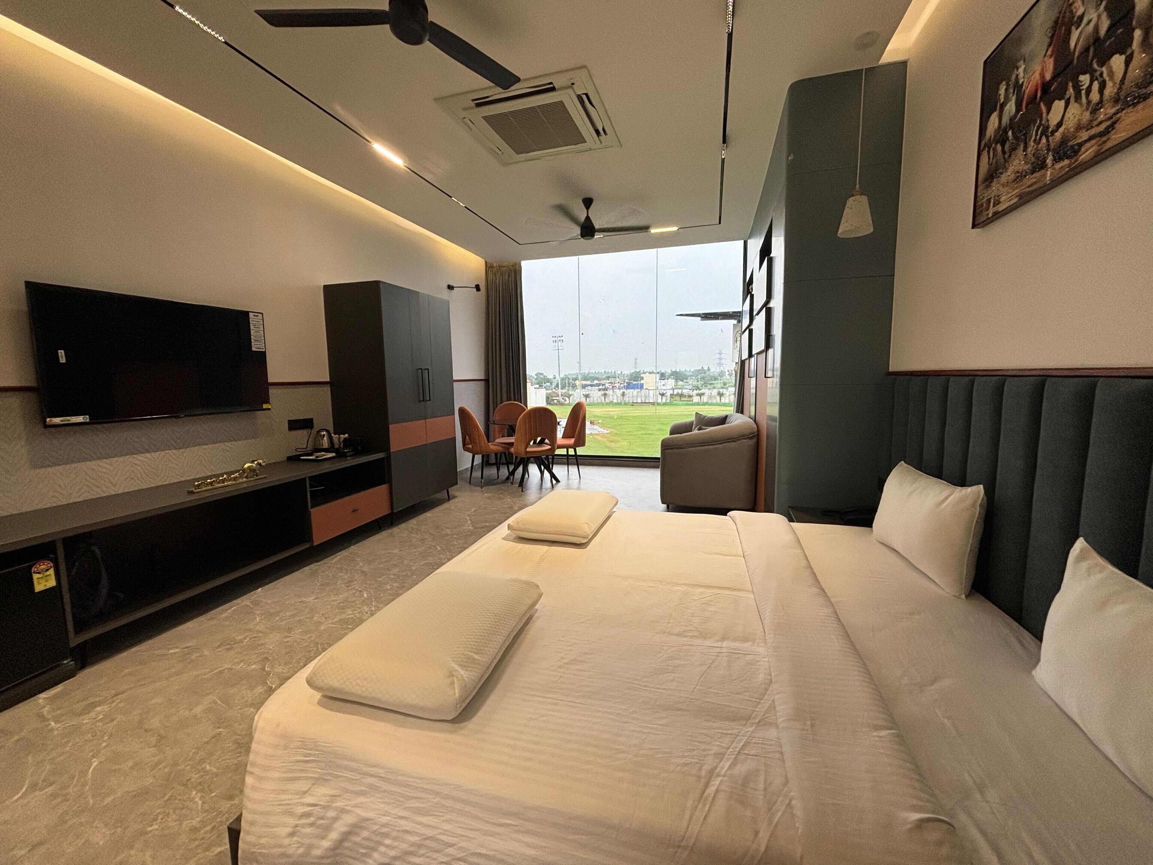 Una habitación de hotel moderna con una cama grande, un televisor de pantalla plana, un escritorio y vista a un campo deportivo.