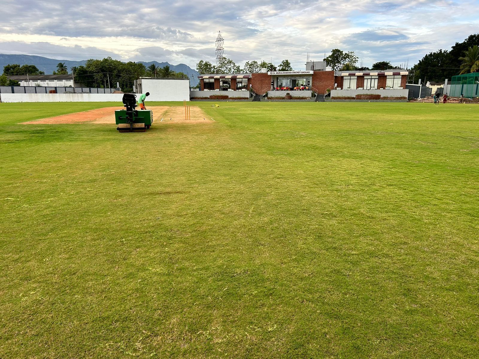 Ein Cricketplatz mit einem gepflegten Rasenfeld, einem Wicket und einer grünen Maschine, vermutlich zum Bowling-Training.
