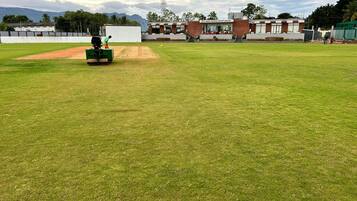 Ein Cricketplatz mit einem gepflegten Rasenfeld, einem Wicket und einer grünen Maschine, vermutlich zum Bowling-Training.