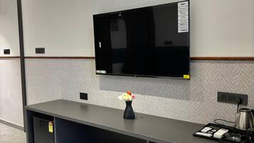Una habitación de hotel moderna con un televisor de pantalla plana montado en la pared, un pequeño florero sobre la mesita consola, y una cafetera a un lado.
