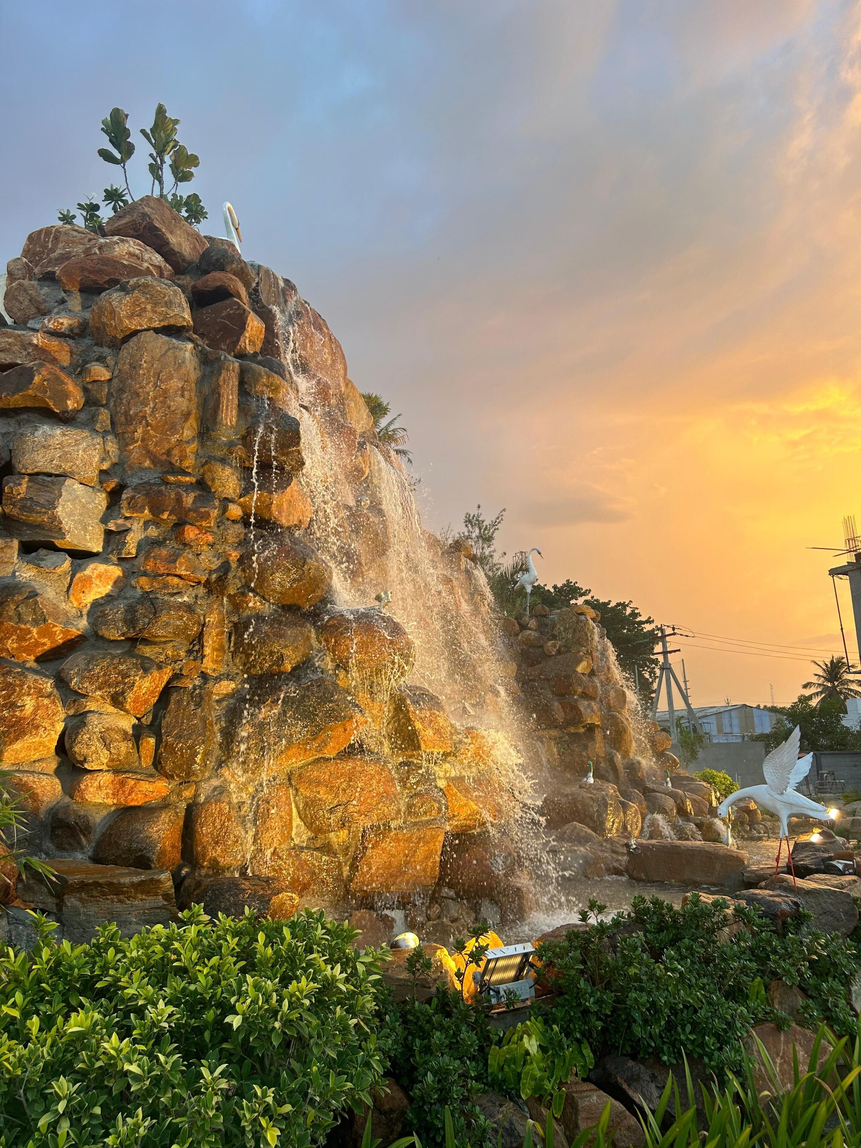 A rock waterfall feature with a statue of a swan, surrounded by greenery.