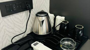 Quarto de hotel com uma mesa preta que acomoda uma cafeteira, duas chávenas, um copo, um comando e um termóstato.