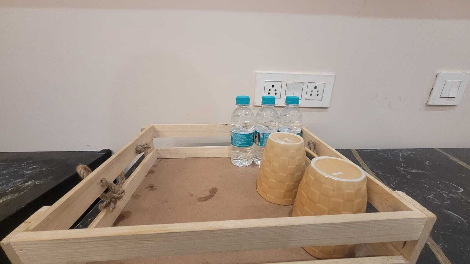 Una bandeja de madera con dos vasos de papel marrón y tres botellas de plástico transparente con tapas azules sobre una superficie negra.