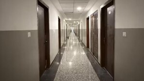 Un long couloir étroit, avec des portes de chaque côté, un sol carrelé et un plafond doté d’un éclairage encastré.