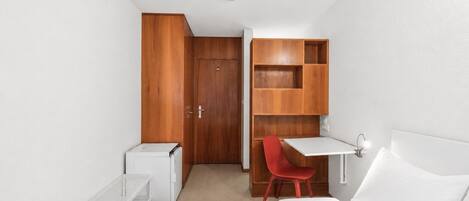 Un dormitorio con cama, escritorio, silla, armario y radiador.