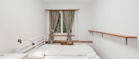 Une chambre à coucher comprenant un lit, un bureau, une chaise, une fenêtre avec des rideaux et une étagère en bois.