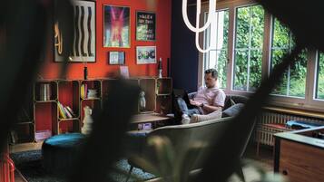 Ein Zimmer mit großem Fenster, einem Bücherregal, einem Schreibtisch und einem Stuhl.