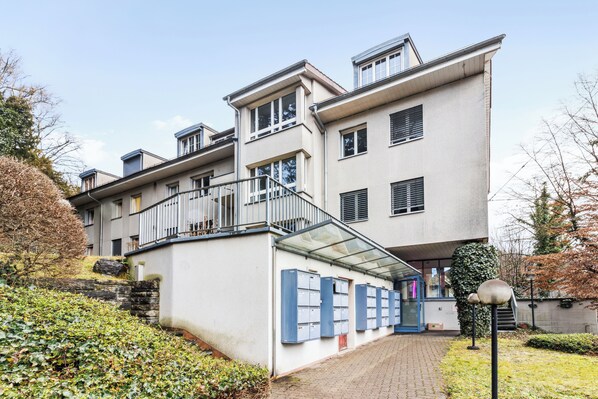 Un immeuble à plusieurs étages doté d’une architecture moderne, avec une entrée en verre, un escalier et une rangée de boîtes aux lettres le long du mur.