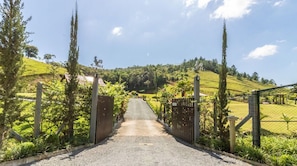 Ein Kiesweg führt zu einem verschlossenen Eingang mit Blick auf eine hügelige Landschaft.