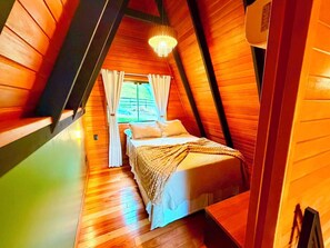 A cozy, triangular room with a bed, a chandelier, and a window with curtains. - Kleines paradies chalés (Blumenau)