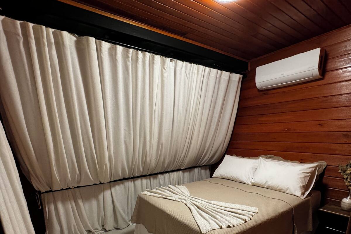 Une chambre à coucher avec un lit, des rideaux, un appareil de climatisation et une table de chevet.