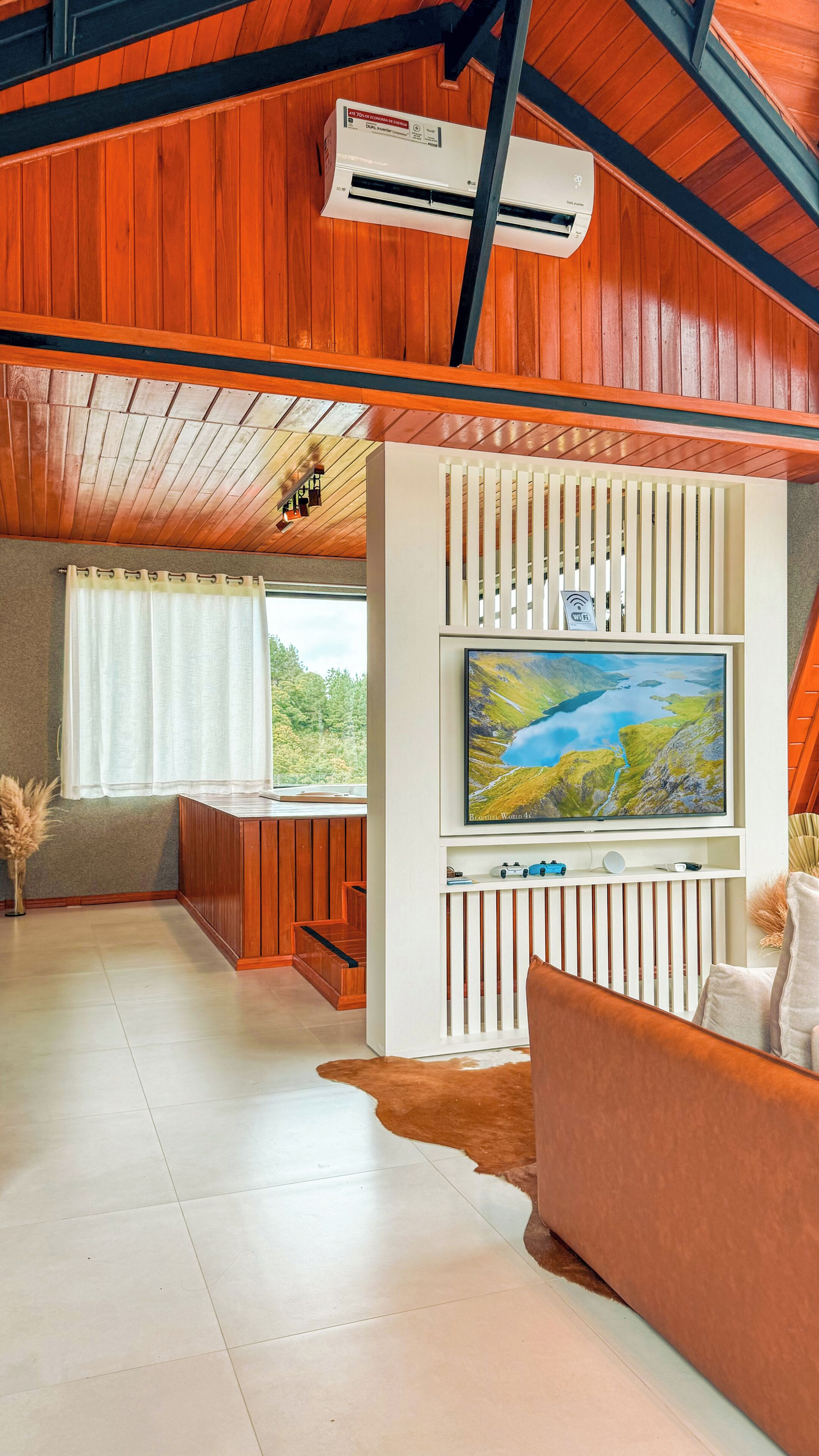 Una sala de estar moderna con un televisor de pantalla plana grande montado en una pared blanca, suelo de madera, un sofá de cuero y un techo con vigas a la vista.