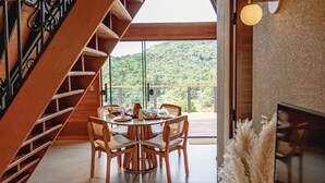 Un comedor con escalera de madera, una mesa con sillas y vistas a un paisaje verde a través de amplios ventanales.