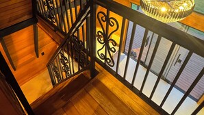 Una escalera de madera con barandal negro que conduce a un balcón con una araña.