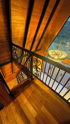 A wooden staircase with a black railing, leading to a balcony with a chandelier. - Kleines paradies chalés (Blumenau)
