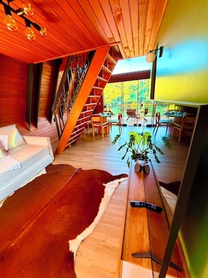 A modern interior with a wooden staircase, a sofa, a dining area, and a view of the outdoors. - Kleines paradies chalés (Blumenau)