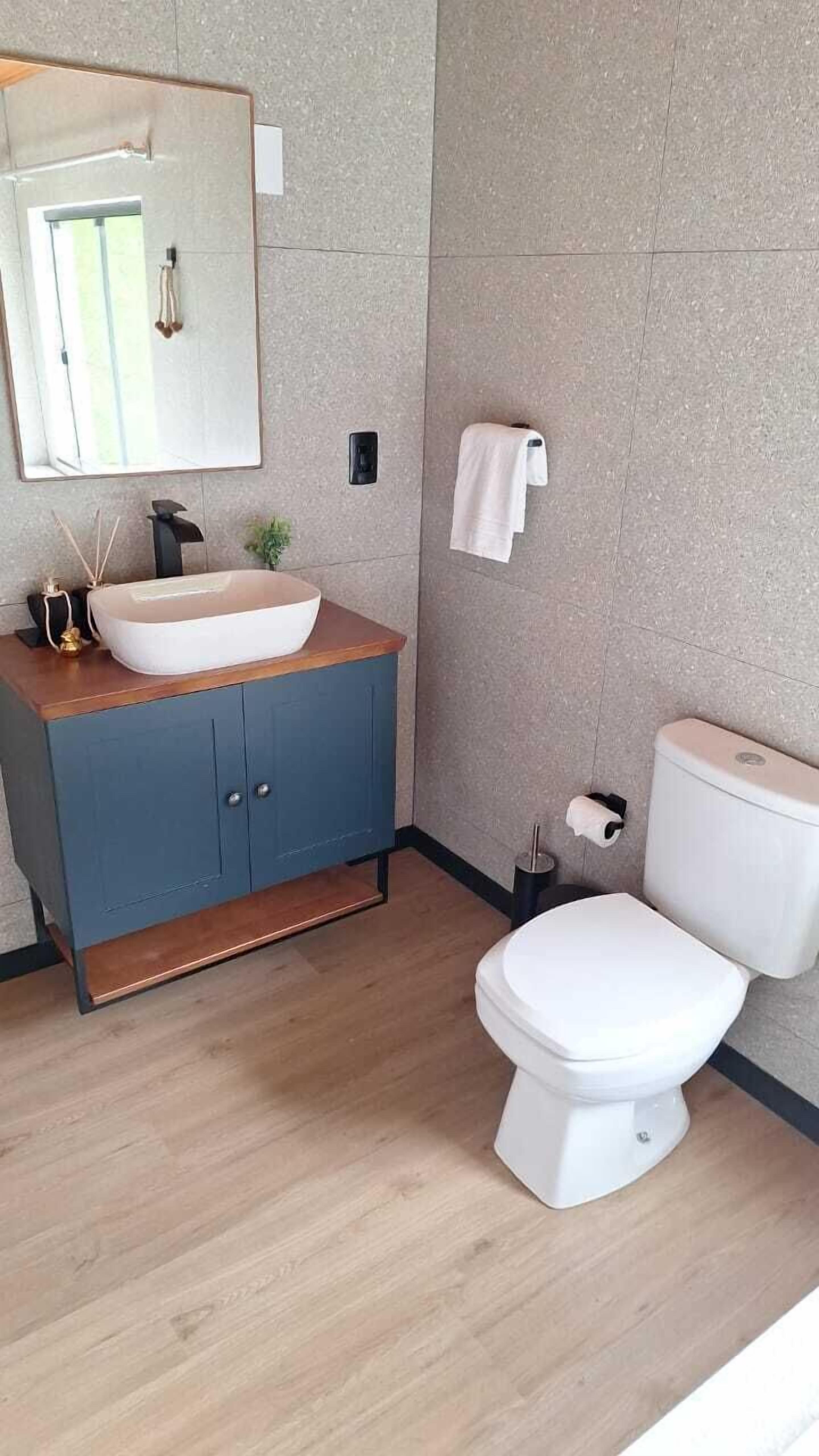 A modern bathroom with a wooden vanity, a white sink, and a toilet.