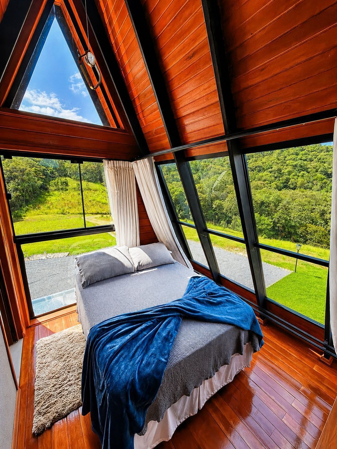 A bedroom with a large window, a bed, and a view of a green landscape.