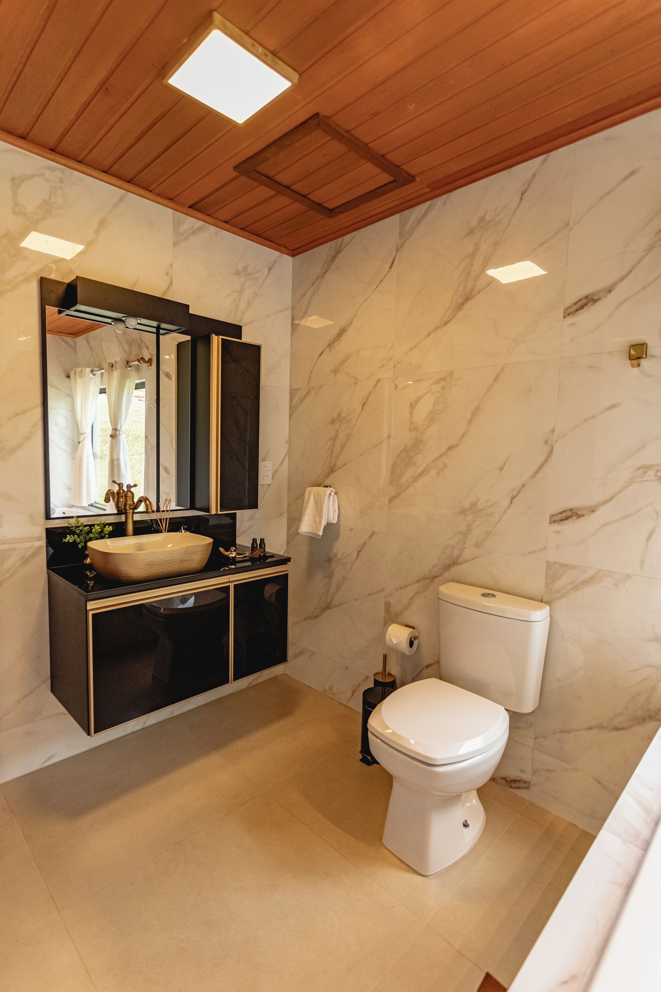 A modern bathroom with a wooden ceiling, marble walls, a large sink, and a toilet.