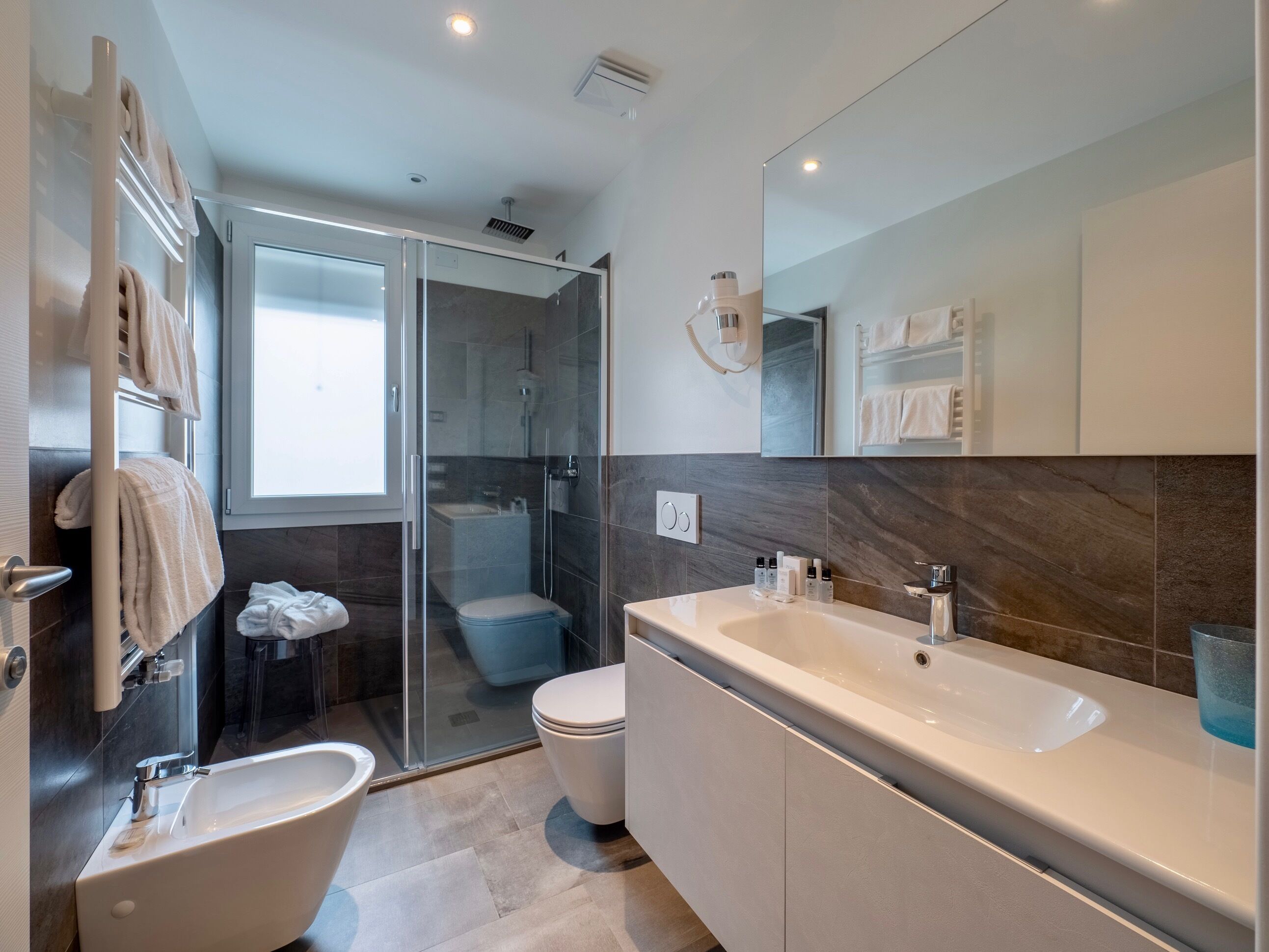 A modern bathroom with a glass shower enclosure, a separate toilet, a large bathtub, and a vanity with a mirror.