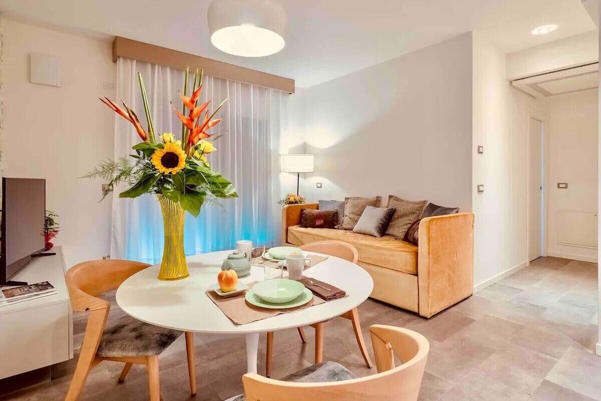 A modern living room with a round dining table, a sofa, and a large window with curtains.