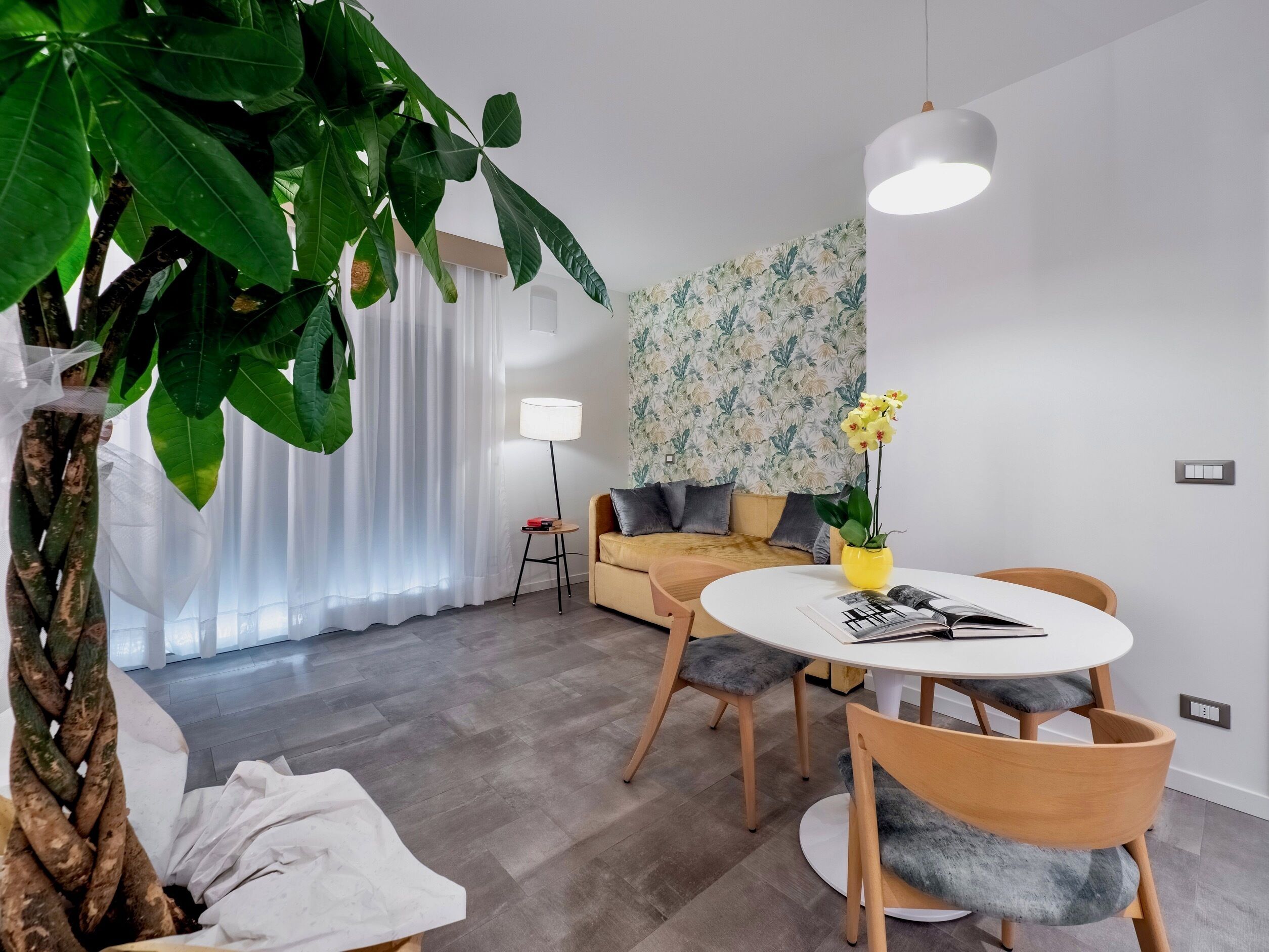 Ein modernes Wohnzimmer mit einem runden Esstisch, Holzstühlen, einer Couch und einer großen Topfpflanze.